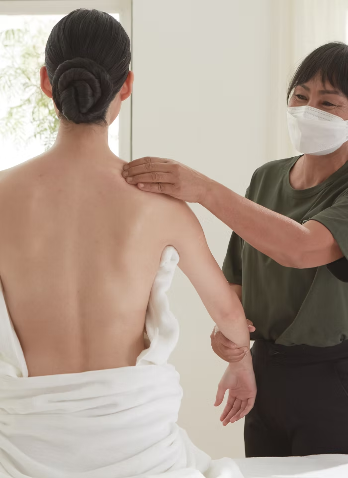 A calm therapist places hands on a guest's shoulder before treatment